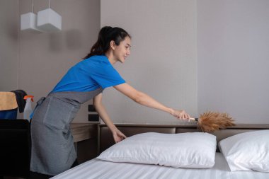 Güzel, genç bir hizmetçi turuncu prezervatifle ev işi yapıyor ve odadaki eşyaları temizlemek için toz bezi kullanıyor...