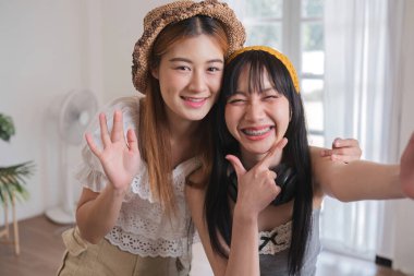 İki kadın gülümsüyor ve poz veriyor. Biri şapka takıyor, diğeri de sarı saç bandı takıyor.