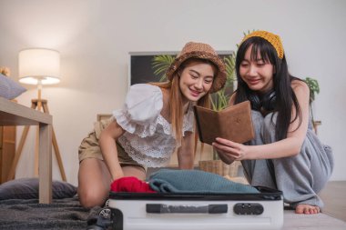 Pasaportları kontrol eden iki kadın yerde, bavulların yanında oturuyorlar..