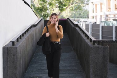 Bir kadın merdivenden inerken cep telefonuyla konuşuyor. O kahverengi bir kazak ve siyah pantolon giyiyor.