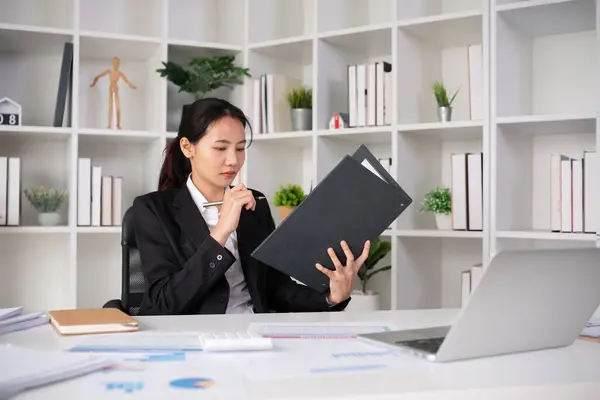 stock image Focused Asian female accountant doing paperwork in office with plan documents on desk.