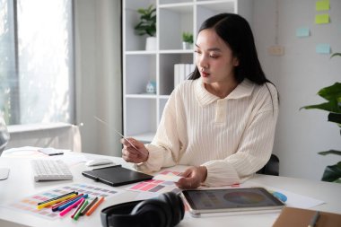 Bilgisayarda grafik tasarımı üzerine çalışan bayan tasarımcı. Oturun ve renklerinizi seçin ve dikkatle ofisinizde çalışın...