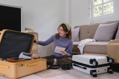 Asyalı kadın tatile çıkmadan önce bavulunu topluyor, eşyalarını, elbiselerini ve seyahat belgelerini topluyor. Yaşam tarzı kavramı.