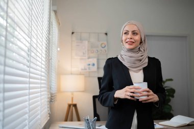 Kendine güvenen Müslüman iş kadını elinde kahve fincanıyla sabahleyin ofisin önünde duruyor..