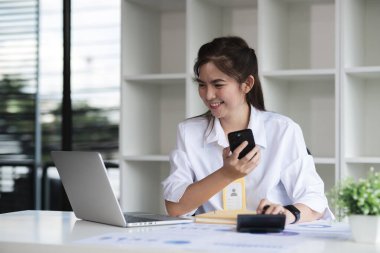 İş kadını beyaz kadın telefonda konuşuyor ve modern ofiste otururken gülümseyerek dizüstü bilgisayar kullanıyor..