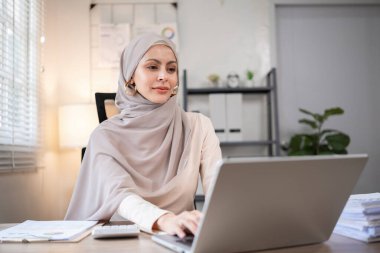 Günümüz iş yerinde çalışan Müslüman iş kadını bilgisayarını kullanarak belgelere not alıyor..