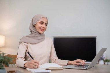 Başörtüsü takan genç bir Müslüman kadın mali hesapları hesaplar. Gelir ve masraflar evdeki oturma odasında..