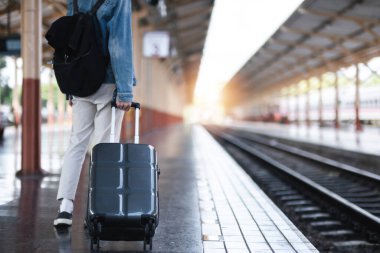 Elinde bavul tutan genç bir adam tren istasyonunda seyahat etmek için bekliyor...