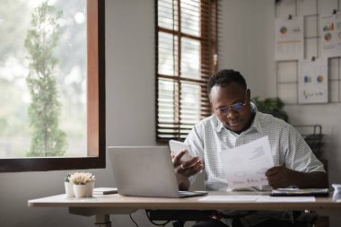 Afro-Amerikalı işadamı evrak işleriyle uğraşıyor, merkez ofiste laptop ile bilgi arıyor..