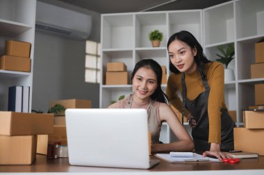 Dizüstü bilgisayarda çalışan ve depoda kutu paketleyen iki kadın..
