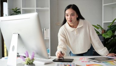 Grafik tasarımı alanında çalışan kadın tasarımcı grafik tasarımı için renk seçin. Bilgisayar üzerinde çalışmak için renkli kağıtlarla dolu bir masaya odaklanmış çalışma.