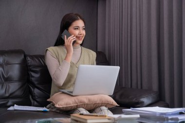 Kanepede dizüstü bilgisayar ve akıllı telefon kullanan bir kadın. Çoklu görev ve modern yaşam tarzı kavramı..