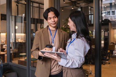 Genç Asyalı iş arkadaşları modern ofis molasında projeyi tabletle tartışıyor.