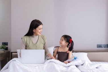 Kızıyla Yatakta Dizüstü bilgisayar kullanan bir kadın. Uzaktan çalışma ve aile zamanı kavramı..