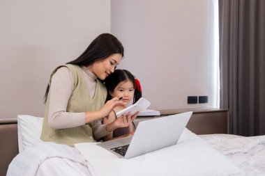 Asyalı anne ve kız ev ödevi olarak dizüstü bilgisayar ve not defteri kullanıyor.