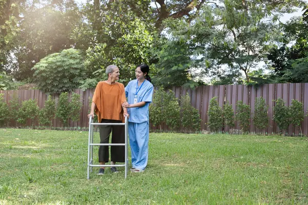 stock image Caregiver helping elderly woman with walker in a green outdoor setting, promoting health, wellness, and supportive living.