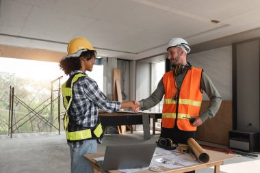 Mühendislik ekibi inşaat yapmayı planlıyor, inşaat alanında el sıkışıyorlar. Modern mimari projelerinde işbirliği ve takım çalışması.