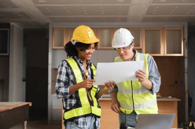 Güvenlik donanımlı iki mühendis bir inşaat alanının planlarını inceliyor, proje detaylarını planlıyor ve tartışıyorlar..