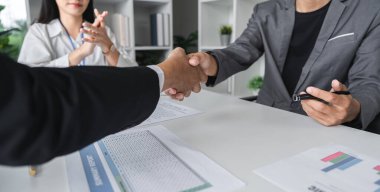 Modern ofis ortamında başarılı bir iş anlaşmasını sembolize eden iki iş adamı el sıkışıyor ve bir sözleşme imzalıyor..