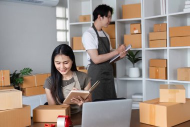 Ofislerinde birlikte çalışan, sipariş alan ve çevrimiçi satışlar için ürün paketleyen bir çift. Etrafı karton kutularla çevrili ve dizüstü bilgisayar kullanıyor..