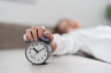 Bir kadın uyanır ve çalar saatini kapatır. Yeni bir günün ve sabah rutininin başlangıcını simgeler..