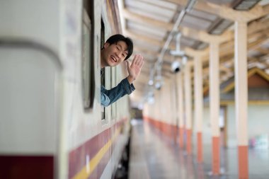 Genç adam platformda duruyor, modern bir tren istasyonunda treni bekliyor, şehir mimarisi ve doğal ışıklandırma sergiliyor..