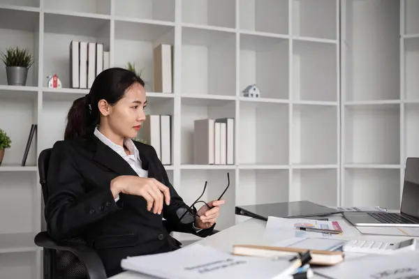 Stock image A young female accountant is seated at her desk, focused on paperwork in a modern office environment.