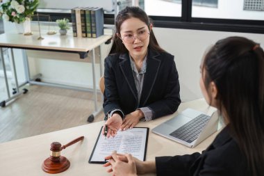 A young lawyer is seen giving professional legal advice to a young woman in a modern office environment, showcasing a professional and supportive atmosphere. clipart