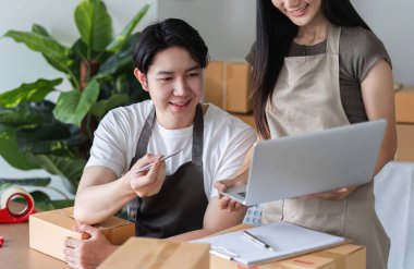 Çevrimiçi küçük işletmelerinde birlikte çalışan neşeli bir çift ürünleri paketliyor ve sipariş ve envanteri yönetmek için dizüstü bilgisayar kullanıyor..