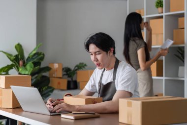 Çevrimiçi işlerini yöneten, sipariş alan, karton kutular ve dizüstü bilgisayarla dolu bir evde ürünleri paketleyen bir çift..