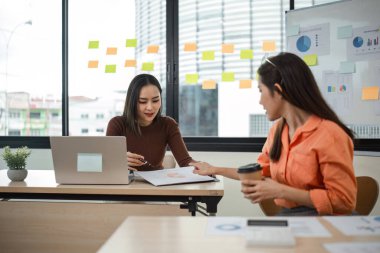 Modern ofis ortamında bir meslektaşımla mali belgeleri inceleyen kadın muhasebeci.