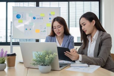 Modern bir ofiste finansal raporlar üzerinde birlikte çalışan iki genç muhasebeci, takım çalışması ve profesyonel ortamlarında başarı sergiliyorlar..