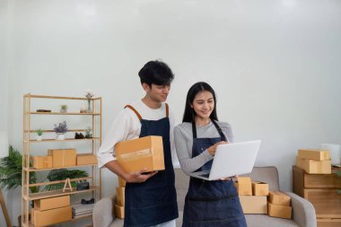 İnternette ürün satmak için birlikte çalışan genç bir çift dizüstü bilgisayar kullanıyor ve evlerinden taşınmak için kutu paketliyorlar..