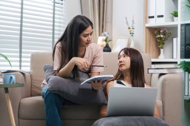 İki genç bayan arkadaş birlikte okuyorlar ve evde online sınavlara giriyorlar, dizüstü bilgisayarlar ve kitaplar kullanıyorlar, destekleyici ve işbirlikçi bir öğrenme ortamı yaratıyorlar..