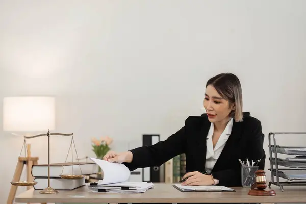 stock image Confident female lawyer in a modern office, reviewing legal documents with scales of justice and gavel on the desk.