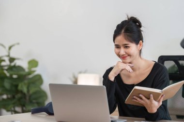 Genç bir kadın evde bilgisayar kullanarak okuyor, e-öğrenim ya da uzaktan eğitim görüyor, modern bir ev ortamında.