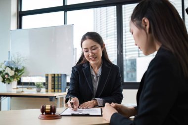 Modern ofis ortamında kadın bir avukat, yasal konuları tartışıyor ve masada tokmağı olan bir müşteriye tavsiyelerde bulunuyor..