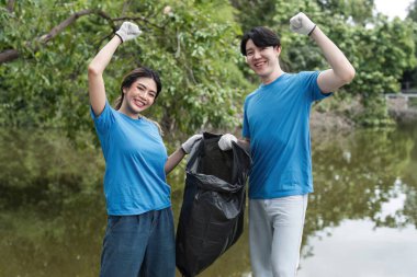 Eldiven ve mavi gömlek giyen hevesli gönüllüler çöpleri doğal ortamda topluyorlar, çevresel koruma ve toplum temizliğine katkıda bulunuyorlar..