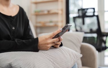Bir kadın, modern bir oturma odasında akıllı telefonunu kullanarak koltukta rahatça oturabilir..