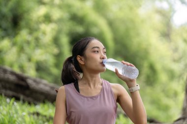 Genç bir kadın bahçede su içiyor. Doğa ortasında sağlıklı bir yaşam tarzı ve su ihtiyacını teşvik ediyor..