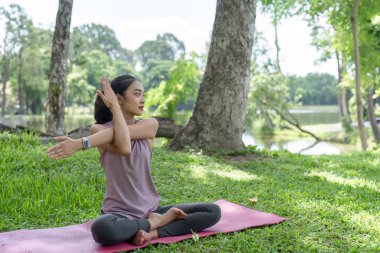 Huzurlu bir park ortamında yoga yapan genç bir kadın sağlıklı bir yaşam tarzı, farkındalık ve açık hava sporu sergiliyor..