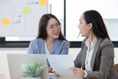 Modern bir ofiste finansal belgeleri tartışan iki kadın muhasebeci, takım çalışması ve profesyonel işbirliği sergiliyorlar..