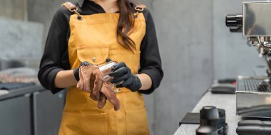 Sarı önlük ve eldiven giyen bir kahve dükkanı çalışanı modern bir kafede endüstriyel dekoru olan camları parlatıyor..