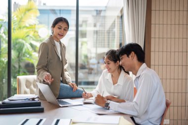 Geniş pencereli ve doğal ışıklandırmalı parlak, modern bir ofis alanında fikirleri tartışan ve paylaşan çeşitli iş adamları..