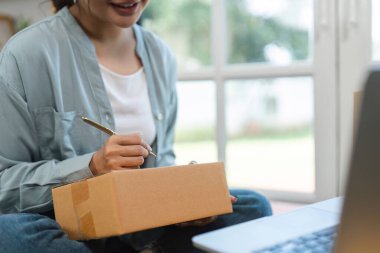 Evde çalışan genç bir kadın, küçük online satış işini yönetiyor. Bir pakete yazıyor, sevkiyata hazırlanıyor..