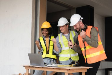 Çeşitli mühendislik ekipleri çalışma planlarını bir inşaat sahasında tartışır, dizüstü bilgisayar kullanır, güvenlik ekipmanları giyer, takım çalışması ve işbirliği yapar..