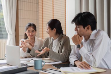 Modern ofis ortamında çalışma hakkında etkin bir şekilde tartışan ve danışmanlık yapan bir iş ekibi, dizüstü bilgisayar ve belgelere sahip.