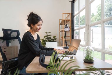 Genç muhasebeci ofisteki mali belgeler üzerinde çalışıyor. Laptop, modern iç mekan ve büyük pencerelerden yansıyan doğal ışık..