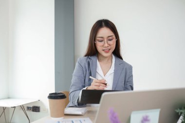 Genç bir kadın muhasebeci, bir dizüstü bilgisayar kullanarak ve bir fincan kahvenin tadını çıkararak, modern bir ofiste finansal belgelerle çalışmaya odaklanmış durumda..