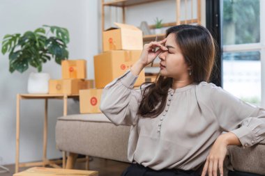 Sevkiyat kutuları ve paketlerle çevrili genç bir kadın, çevrimiçi satışları yönetirken stresli görünüyor..